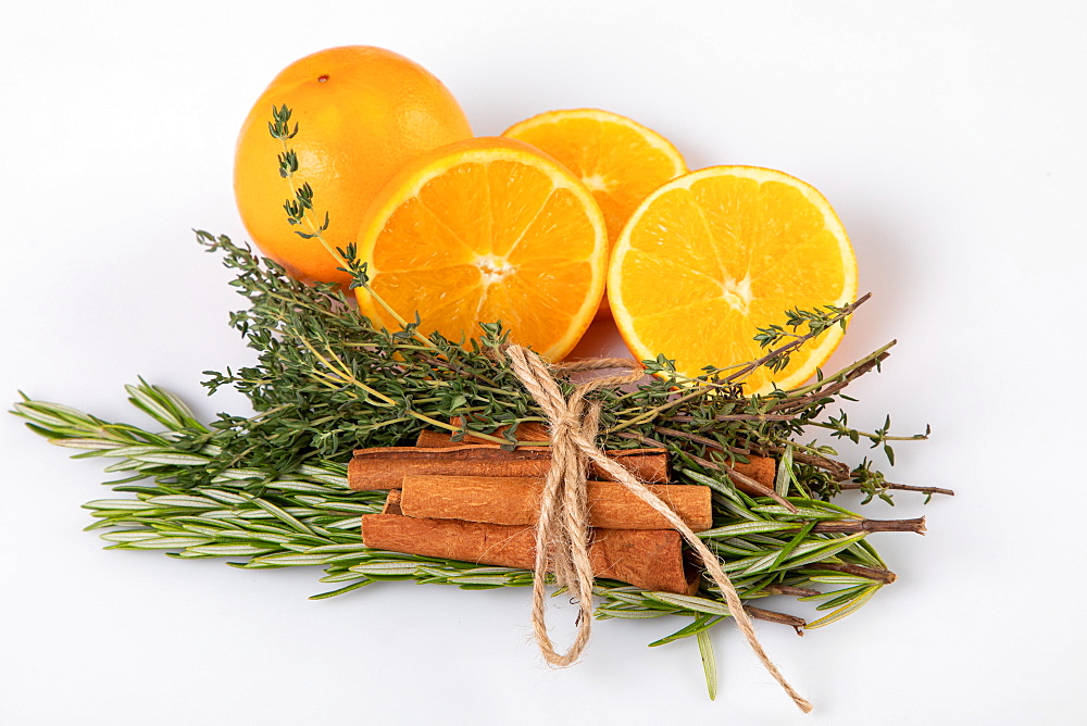 Fresh oranges with cinnamon sticks tied together with rosemary and thyme, white background