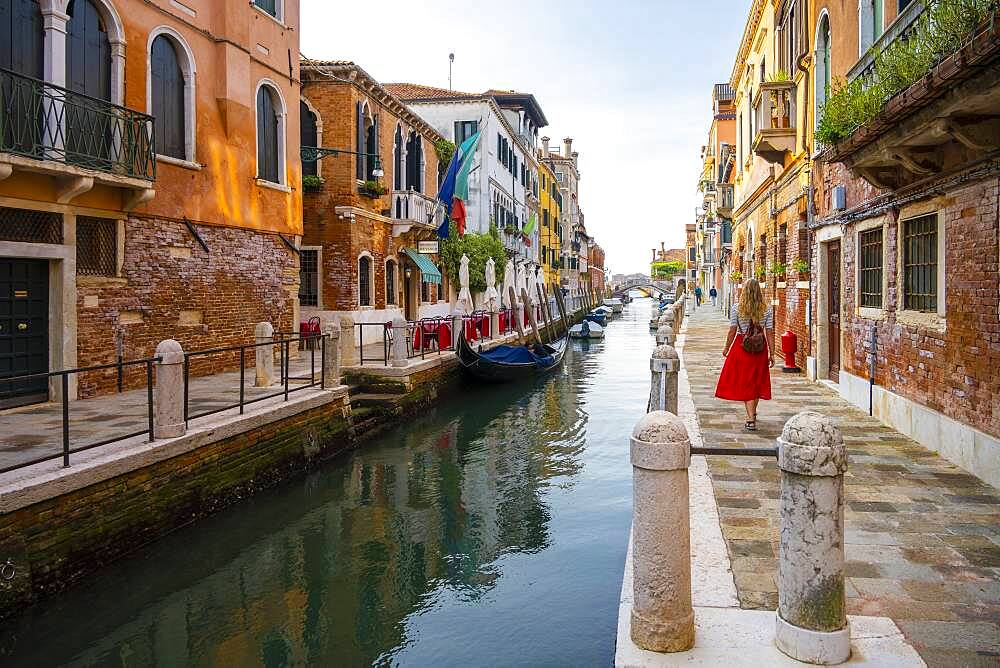 Young woman with red skirt walks between canal and old houses, Venice, Veneto, Italy, Europe