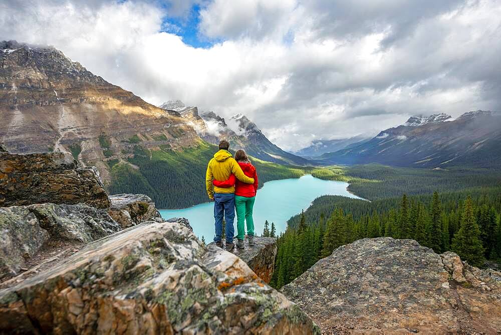 Couple hugging, looking into the distance, view of turquoise glacial lake surrounded by forest, Peyto Lake, Rocky Mountains, Banff National Park, Alberta Province, Canada, North America