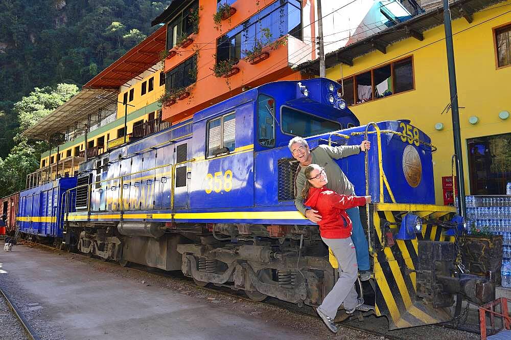 Two tourists at the locomotive of the Perurail in the station, Aguas Calientes, Machu Picchu, Urubamba Province, Peru, South America