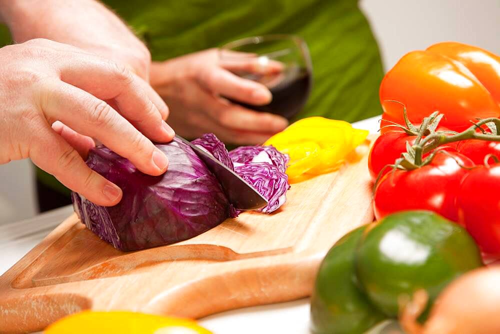 Man slicing vegetables on cutting board while woman enjoys a glass of red wine