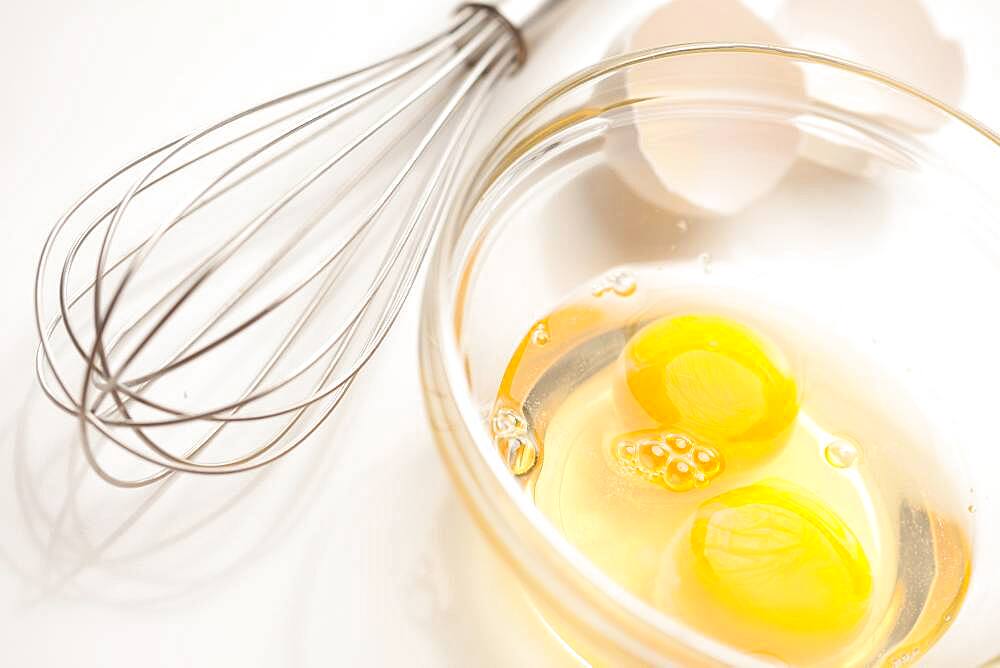 Hand mixer with eggs in a glass bowl on a reflective white background