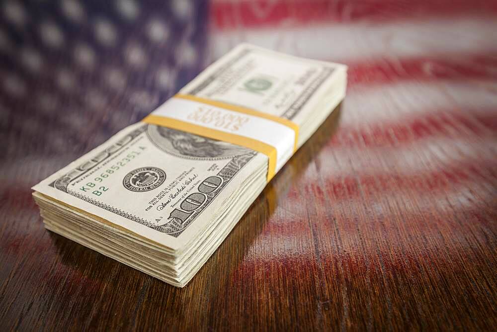 Thousands of dollars stacked with reflection of american flag on wooden table