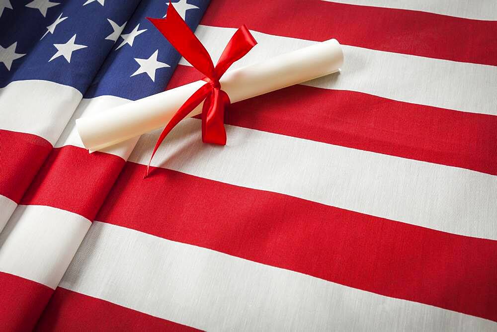 Red ribbon wrapped diploma resting on american flag with copy space