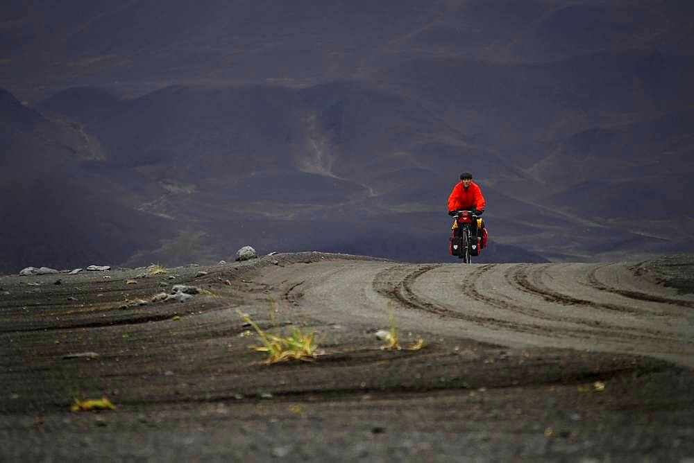 Cyclist, mountain biker with orange jacket, lava desert Krepputunga, highland track Austurleio, Asturleid, F 910, highlands, central Iceland, Iceland, Europe