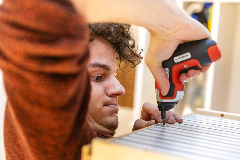 Young man doing DIY in his apartment, assembling a shelf