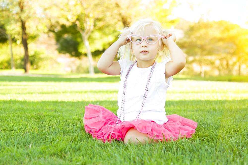 Cute little girl playing dress in the grass up with pink glasses and beaded necklace