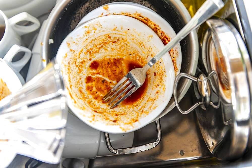 Dirty dishes in a sink, cutlery and plates in a pile, rinsing off