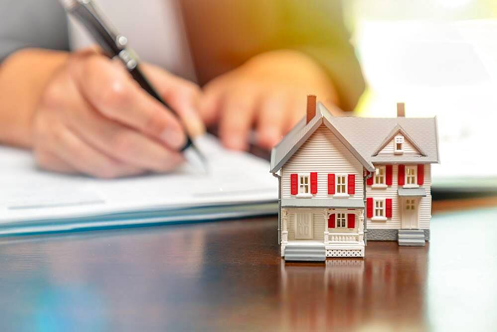 Man signing real estate contract papers with small model home in front