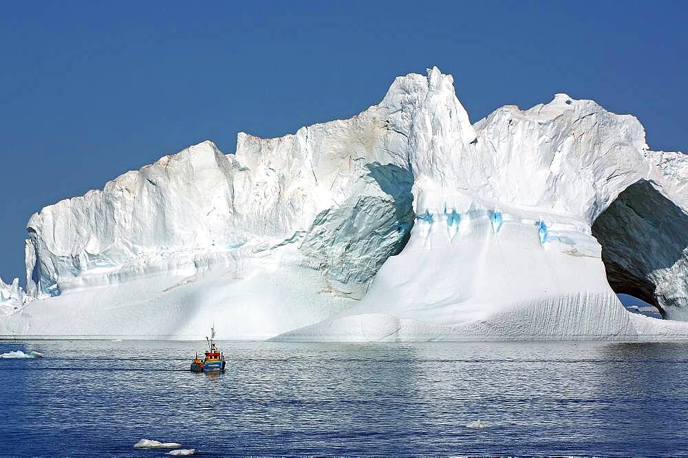 Small fishing boat in front of huge iceberg with two holes, Disko Bay, Ilulissat, Greenland, Denmark, North America