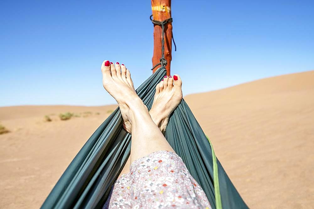 Young woman relaxing in green hammock with view on sand dunes of Sahara Desert, Morocco, Africa
