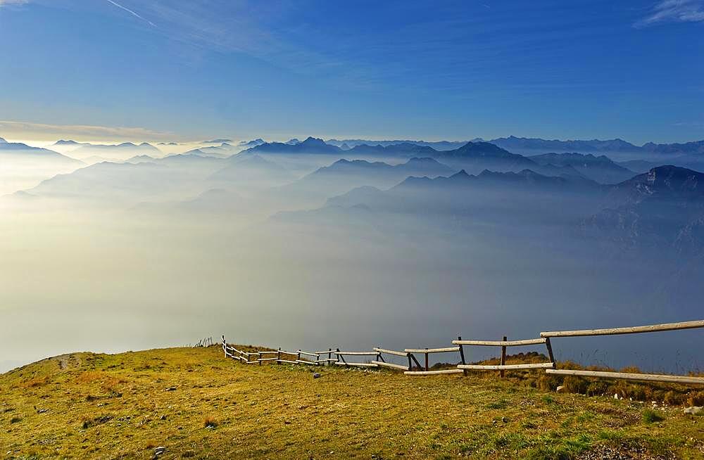 Meadow with fence and Lake Garda in the morning mist with Lake Garda mountains and Bergamo Alps, Monte Baldo, Malcesine, Verona Italy, Trentino-Alto Adige, Italy, Europe