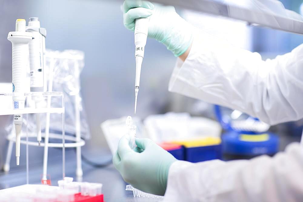 Young lab technician wearing a face mask and pipetting a sample in a laboratory with laboratory equipment at a workflow, Freiburg, Baden-Wuerttemberg, Germany, Europe