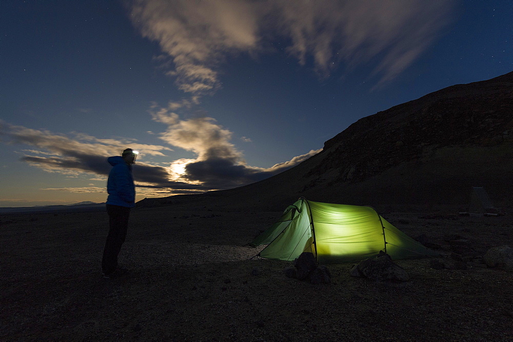 Man with headlamp standing in front of tent lit from inside, moonrise, Askja volcano, Icelandic highlands, Iceland, Europe