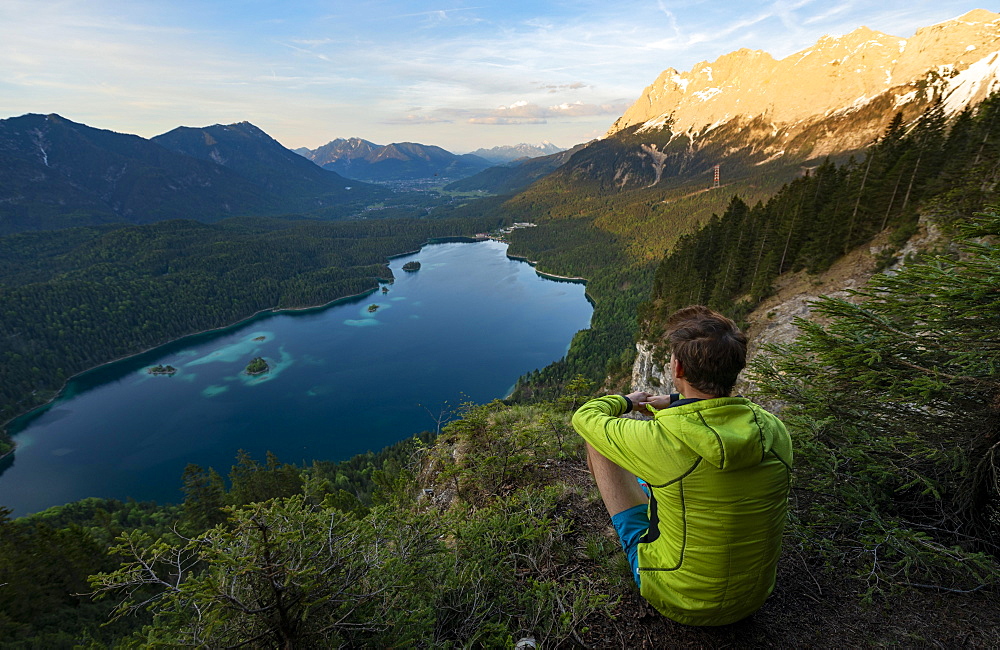 Young man looking over the Eibsee lake at sunset, Zugspitze and Zugspitzmassiv, alpenglow, behind Bishop and Krottenkopf, Wetterstein Mountains, near Grainau, Upper Bavaria, Bavaria, Germany, Europe