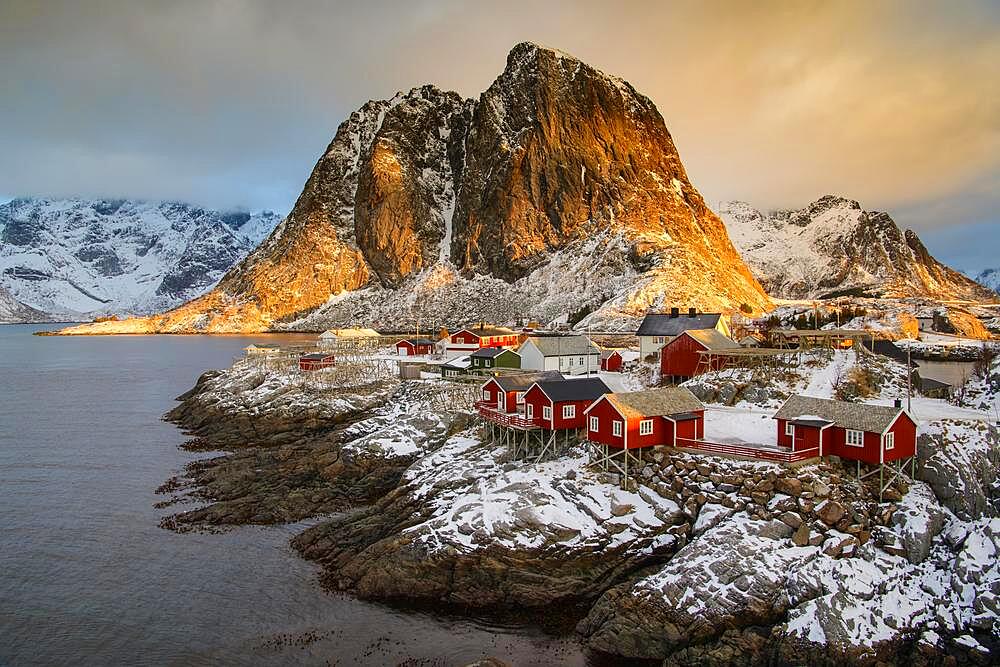 Winter Scandinavian landscape with illuminated red houses, sea, mountains, snow, Hamnoy, Nordland, Lofoten, Norway, Europe