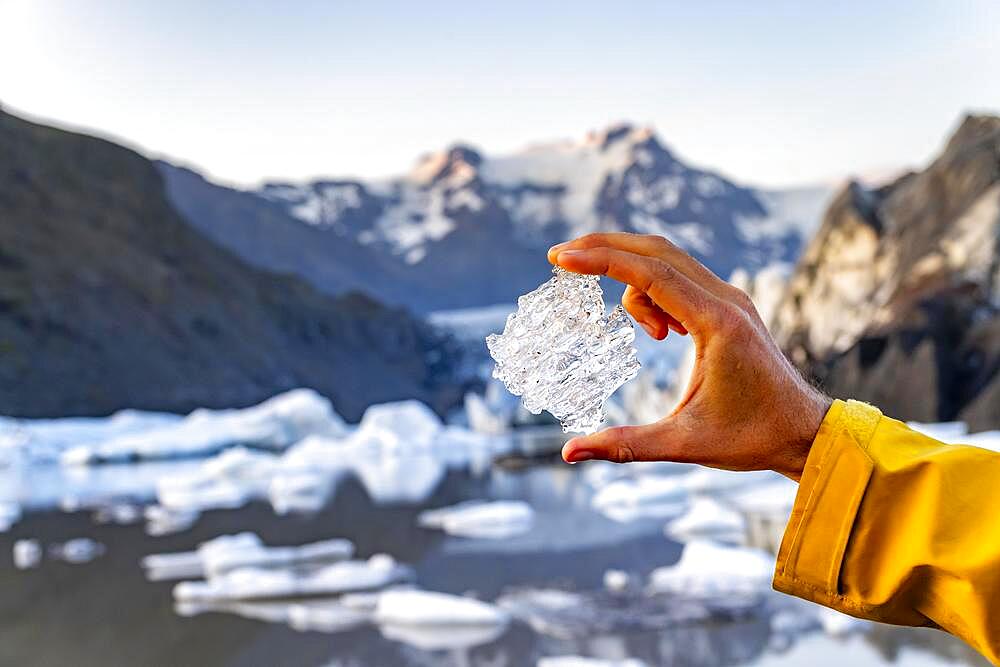 Hand holding glacial ice, Svinafellsjoekull glacier, Hvannadalshnukur mountain behind, Vatnajoekull National Park, Skaftafell, South Iceland, Iceland, Europe