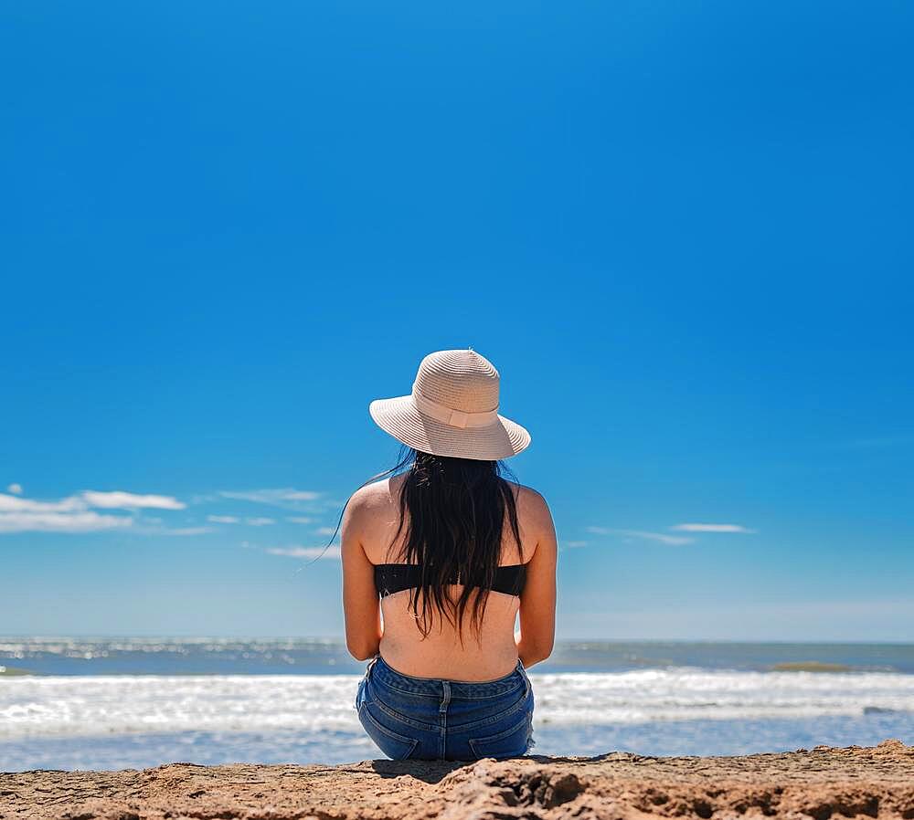 Woman in hat from back to the sea, girl in hat looking to the sea, vacation concept, rear view of a girl watching the sea