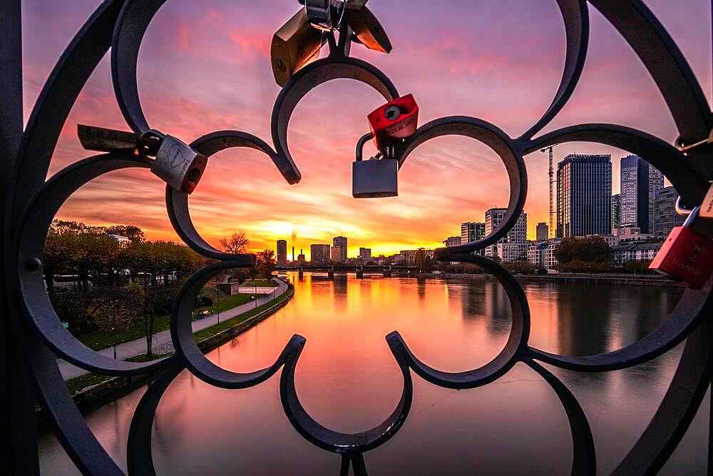 View through a railing with love locks, in the evening with a dreamlike sunset behind the skyline, Frankfurt, hesse, Germany, Europe