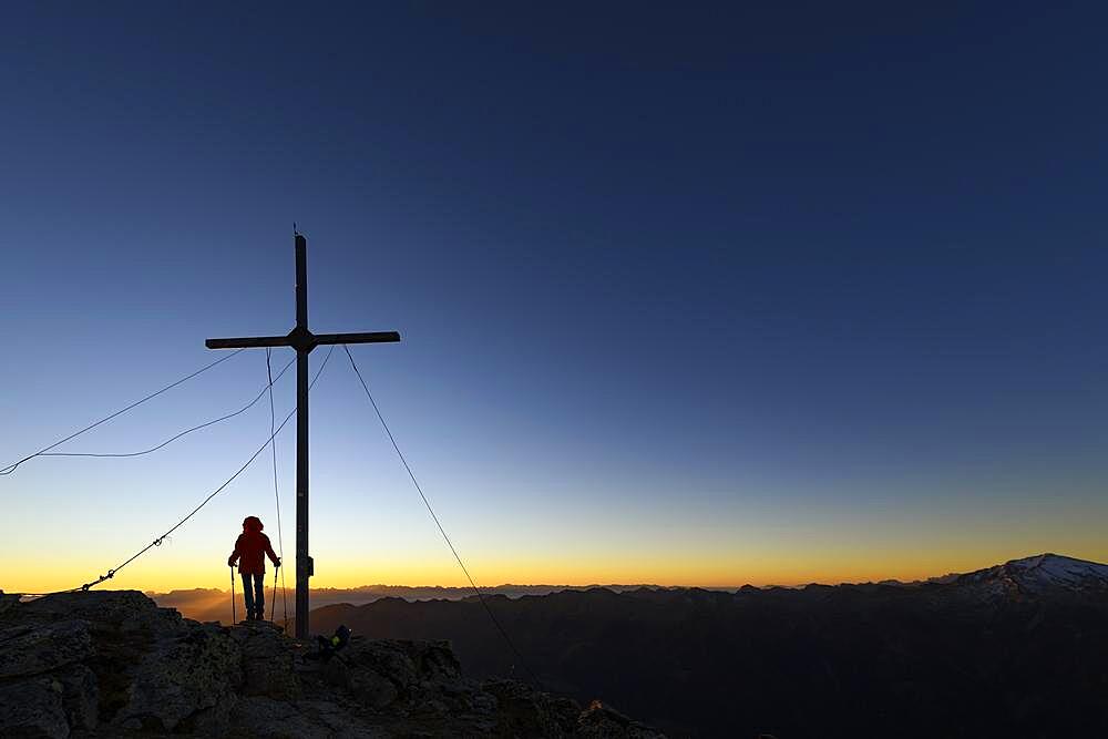 Vermoispitze summit cross with climber at sunrise with South Tyrolean mountains in the background, Naturns, South Tyrol, Italy, Europe