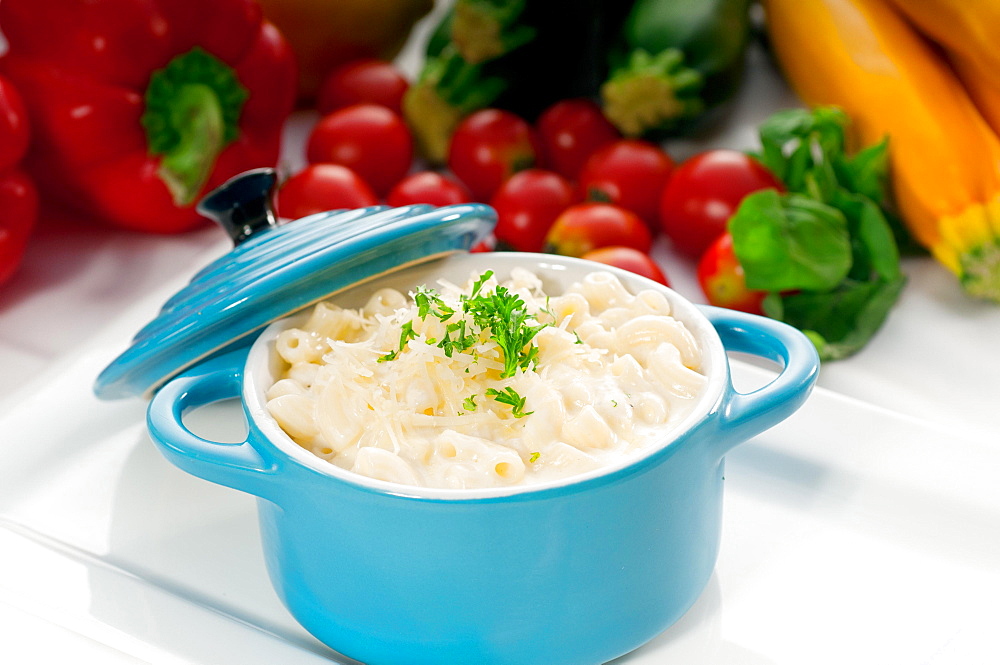 Macaroni and cheese, kids favourite dish, on a blue little childish clay pot with vegetables on background