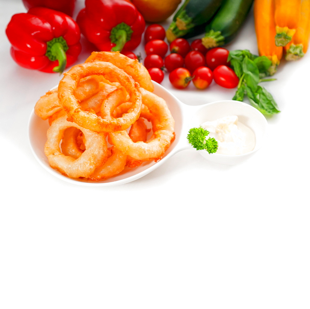 Golden deep fried onion rings served with mayonnaise dip and fresh vegetables oln background