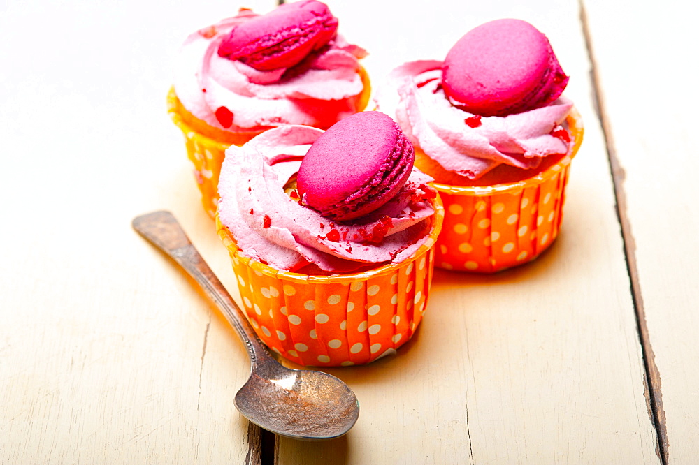 Fresh pink berry cream cupcake with macaroon on top over rustic wood table