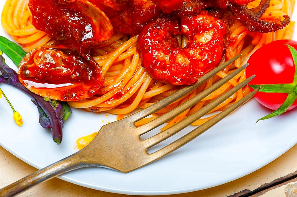 Italian seafood spaghetti pasta on red tomato sauce over white rustic wood table