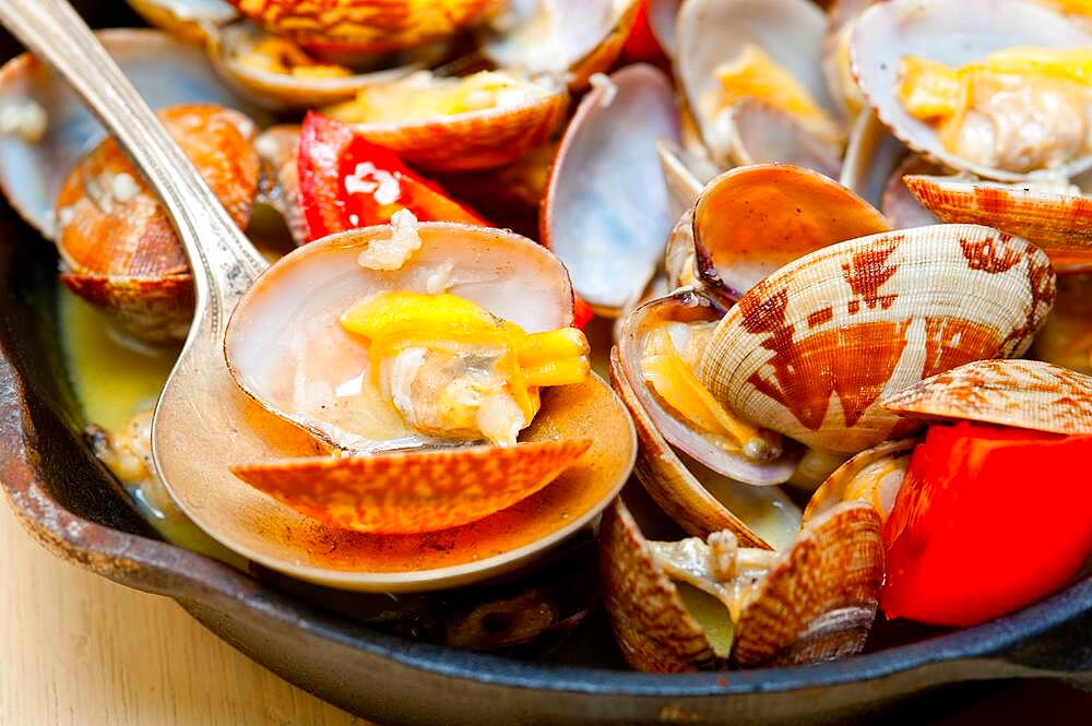 Fresh clams stewed on an iron skillet over wite rustic wood table