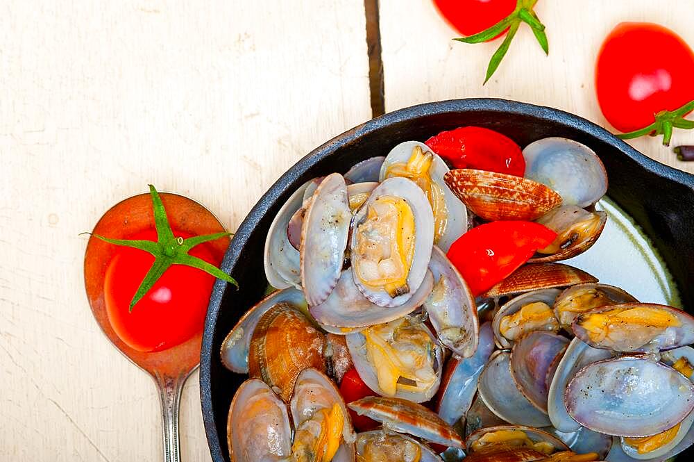 Fresh clams stewed on an iron skillet over wite rustic wood table