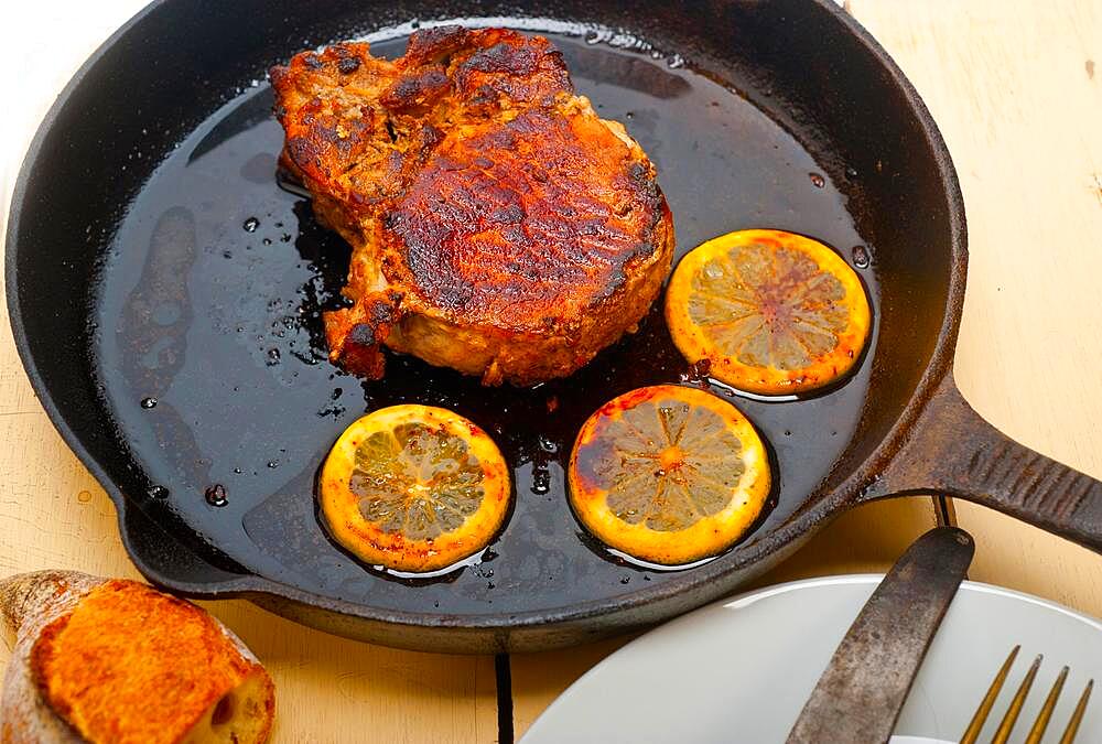 Pork chop seared on iron skillet with lemon and spices seasoning