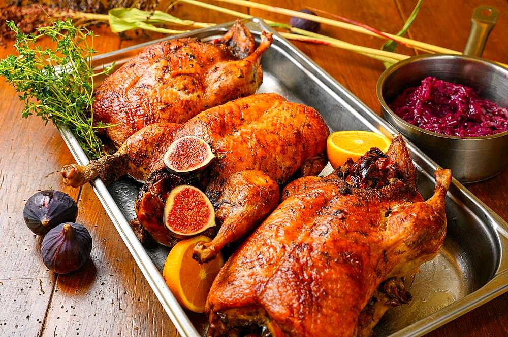 Three crispy brown roasted turkeys (Meleagris gallopavo Linnaeus f. domestica) with vegetable cabbage (Brassica oleracea var. capitata f. rubra) on a wooden table