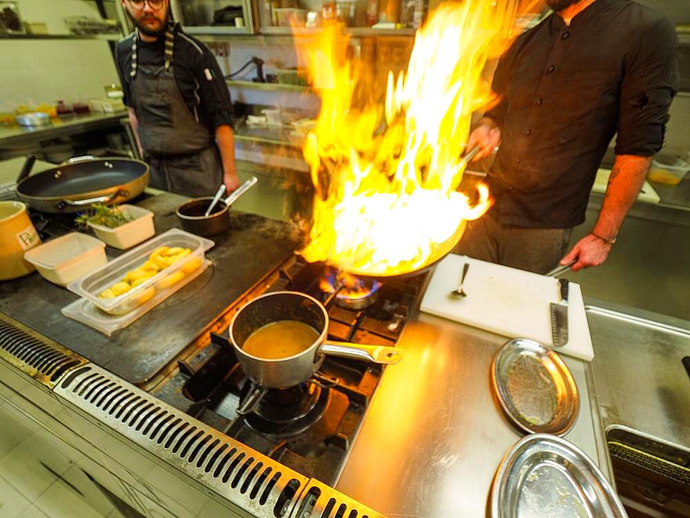 Chef cooking flambleing atlantic squid with olive oil in a big pan in a professional kitchen, trendy seafood recipe, Professional gourmet cooking concept