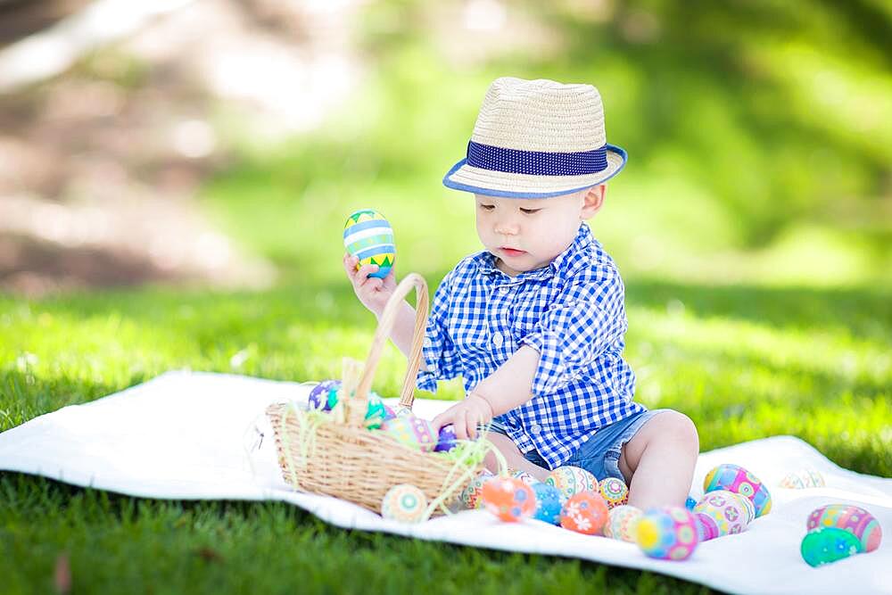 mixed-race chinese and caucasian baby boy outside wearing rabbit ears playing with easter eggs