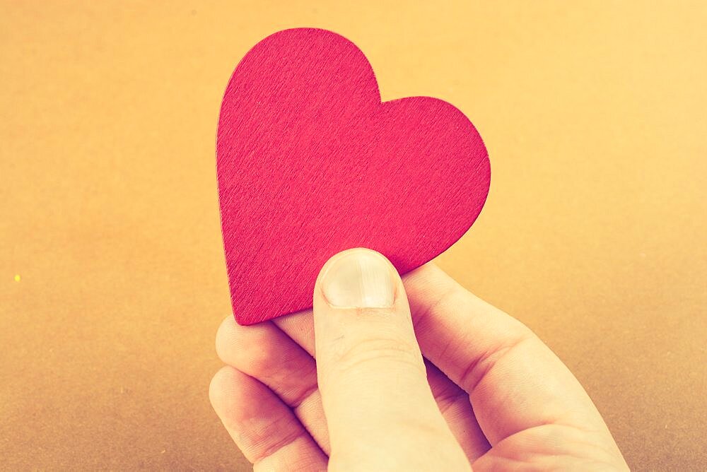 Red color heart shaped object in hand on dotted paper