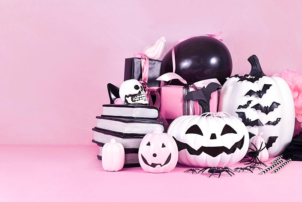 Pink Halloween decor with black and white pumpkins, spell books and spiders with copy space