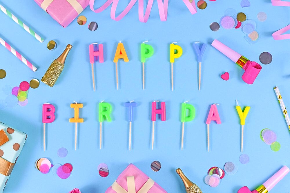 Letter canles forming text Happy Birthday with confetti and paper streamers on blue background