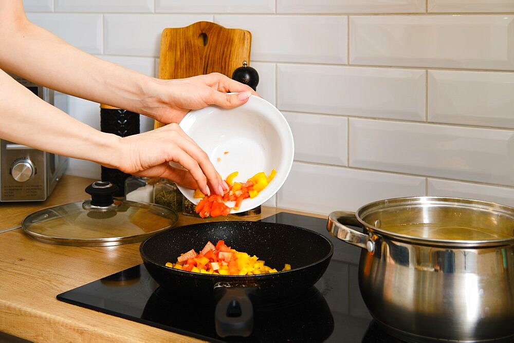 Closeup view of female hand puts chopped vegetables in a frying pan. Process of preparation of vegetable gravy