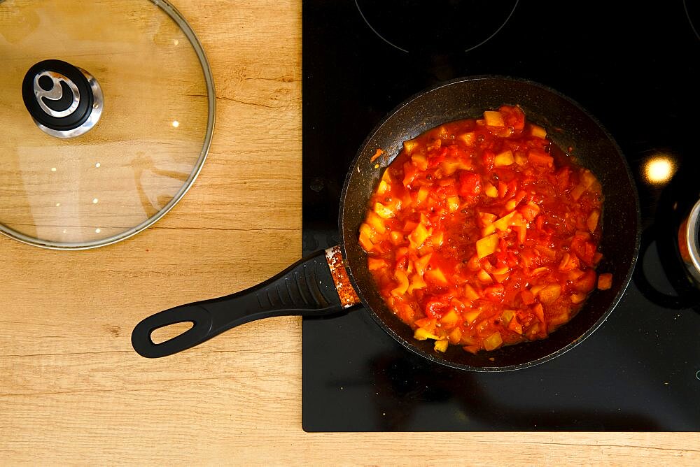 Overhead view of frying pan with tomato sauce on modern electric stove, the glass lid lies next to it