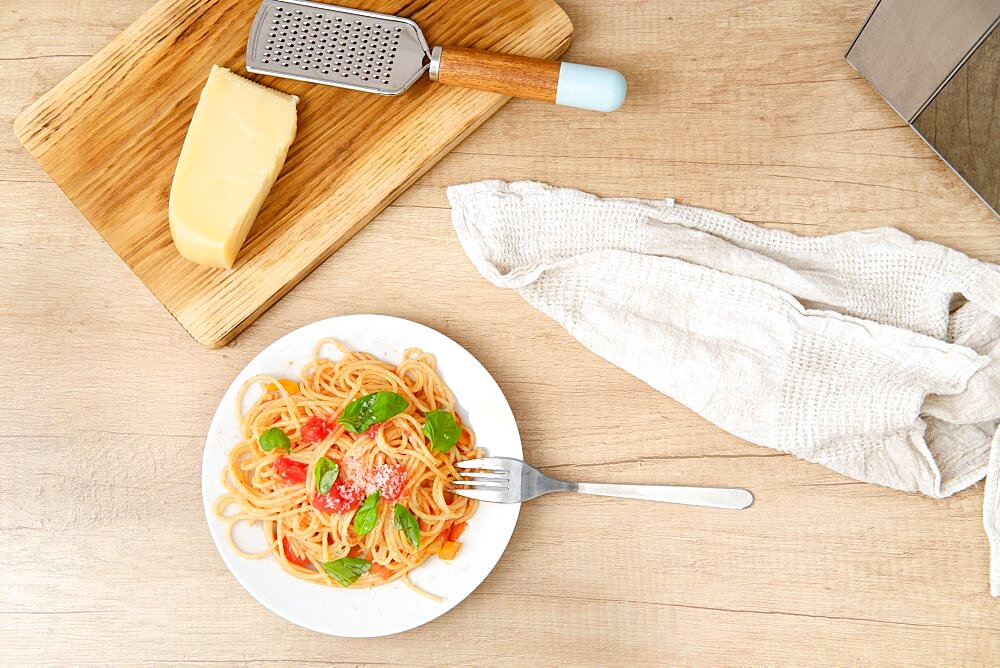 Overhead view of a plate with prepared spaghetti with vegetable sauce and basil. View from above at food on kitchen tabletop