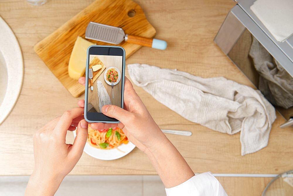 View from above of unrecognizable woman with smartphone taking photo of plate with pasta with tomato sauce for culinary blog at home. Food blogger recording video of ready spaghetti