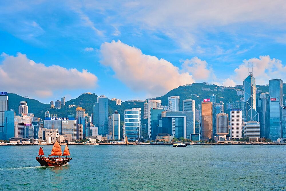 HONG KONG, CHINA, MAY 1, 2018: Hong Kong skyline cityscape downtown skyscrapers over Victoria Harbour with tourist junk boat on sunset. Hong Kong, China, Asia