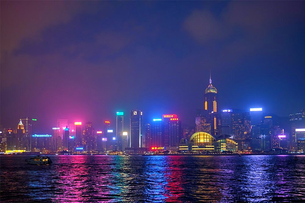 HONG KONG, CHINA, APRIL 28, 2018: Hong Kong skyline cityscape downtown skyscrapers over Victoria Harbour in the evening illuminated with tourist boat ferries, Hong Kong, China, Asia