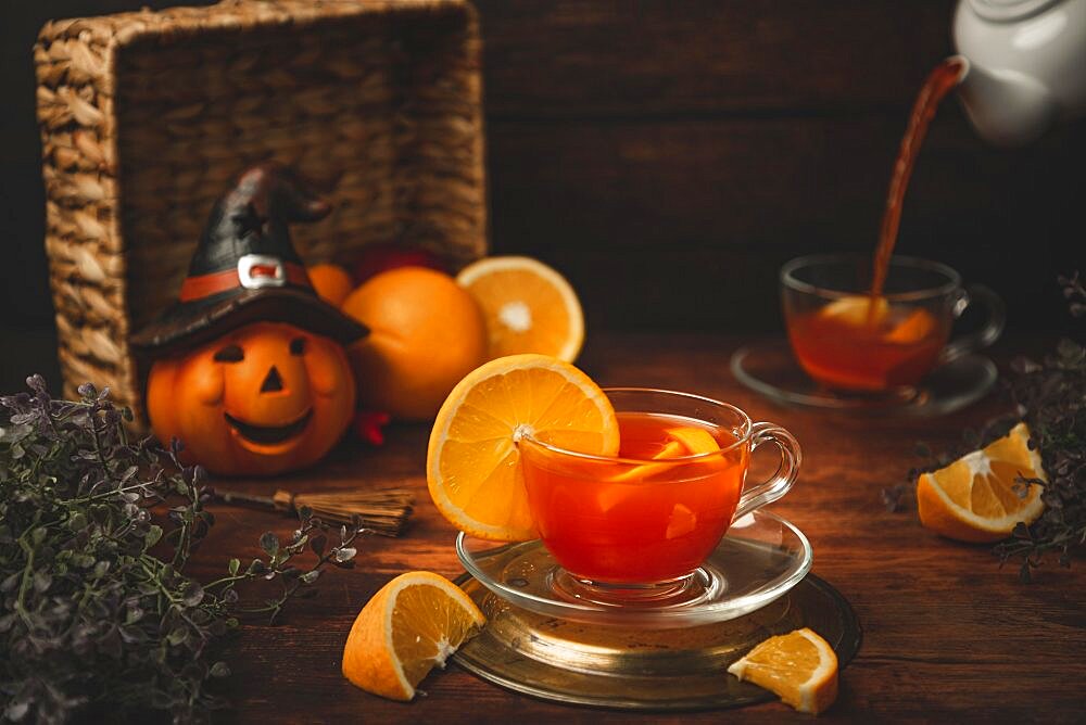 Tea with orange in cup, on wooden background, in front of Halloween decoration