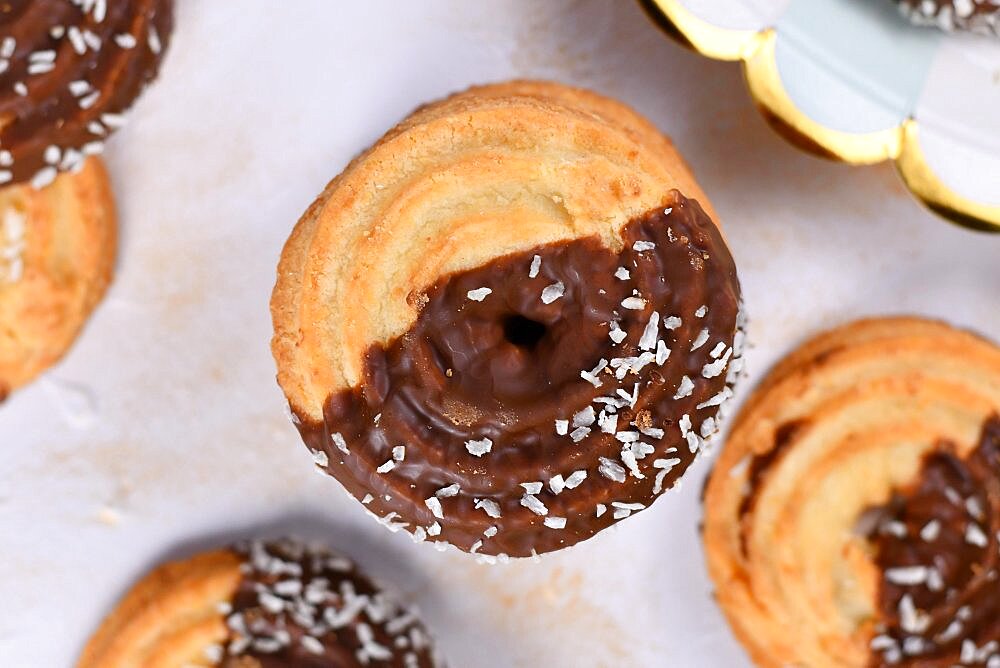 Round ring shaped spritz biscuits with half side glazed with chocolate and topped with coconut sprinkles