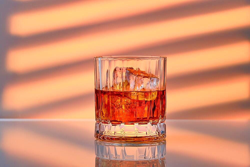 Whiskey with ice in facetted rocks glass over striped background