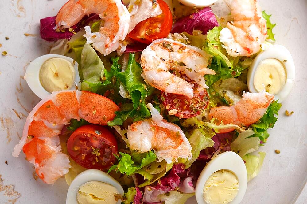 Vegetable salad with quail egg and shrimps, seasoned with oil, on a white plate