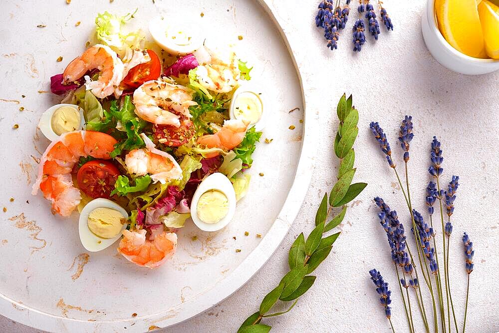 Vegetable salad with quail egg and shrimps, seasoned with oil, on a white plate