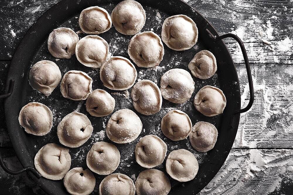 Handmade homemade dumplings on a decorative metal tray on a wooden background with flour. Diy meat dumplings