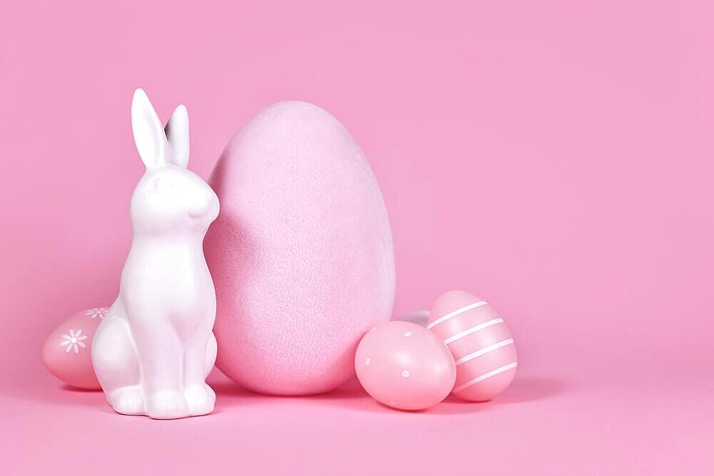 White bunny sculpture with easter eggs on pink background with copy space